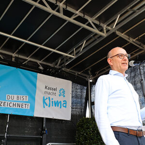 Andreas Ernst auf der Bühne vor einem Standmikrofon, das blaue Banner des Klimaschutzpreises im Hintergrund