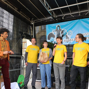 Moderator und das Team mit 5 Personen von SoLocal Energy mit gelben T-Shirts und aufgedrucktem blauen Schriftzug des Vereins auf der Bühne, im Hintergrund das blaue Banner des Preises