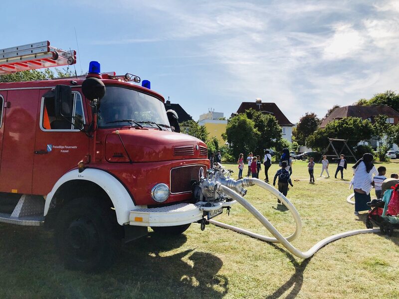 Feuerwehrauto mit spielenden Kindern im Hintergrund