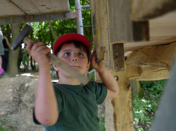 Kleiner Junge hämmert einen Nagel in ein Stück Holz