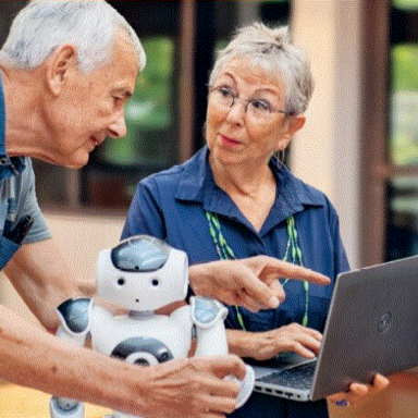 Zwei Senioren, einer hat einen Roboter in der Hand, die andere einen Laptop