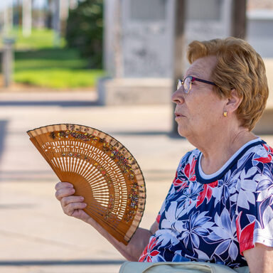 Ältere Frau sitzt draußen mit Fächer