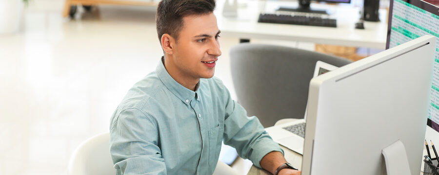 Ein junger Mann sitzt im Büro vor dem Computer und programmiert.