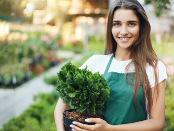 Portrait of young european female garden owner holding a plant running a successful online gardening shop