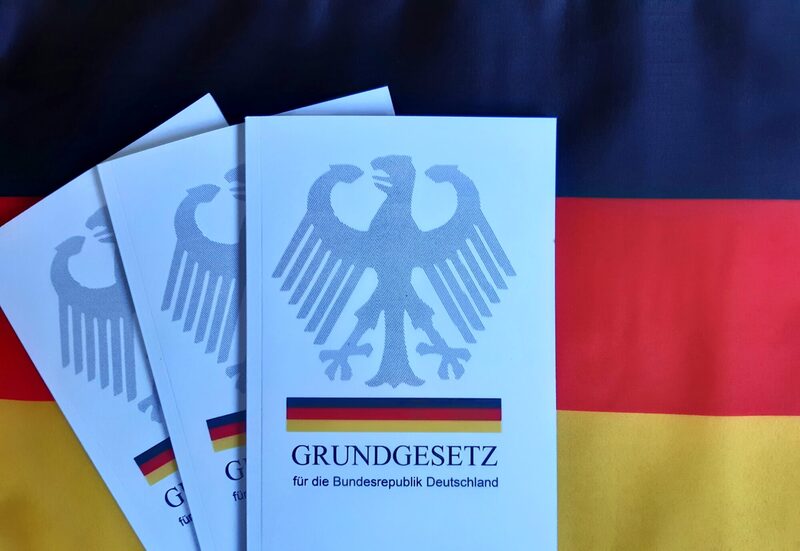 Drei Ausgaben des GG vor der deutschen Flagge.