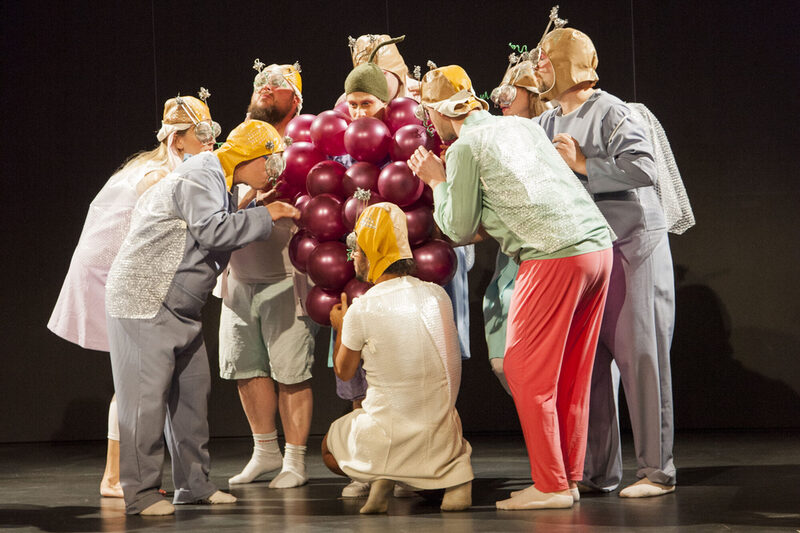 Theatergruppe die sich um eine lebensgroße Weintraubenrebe schart