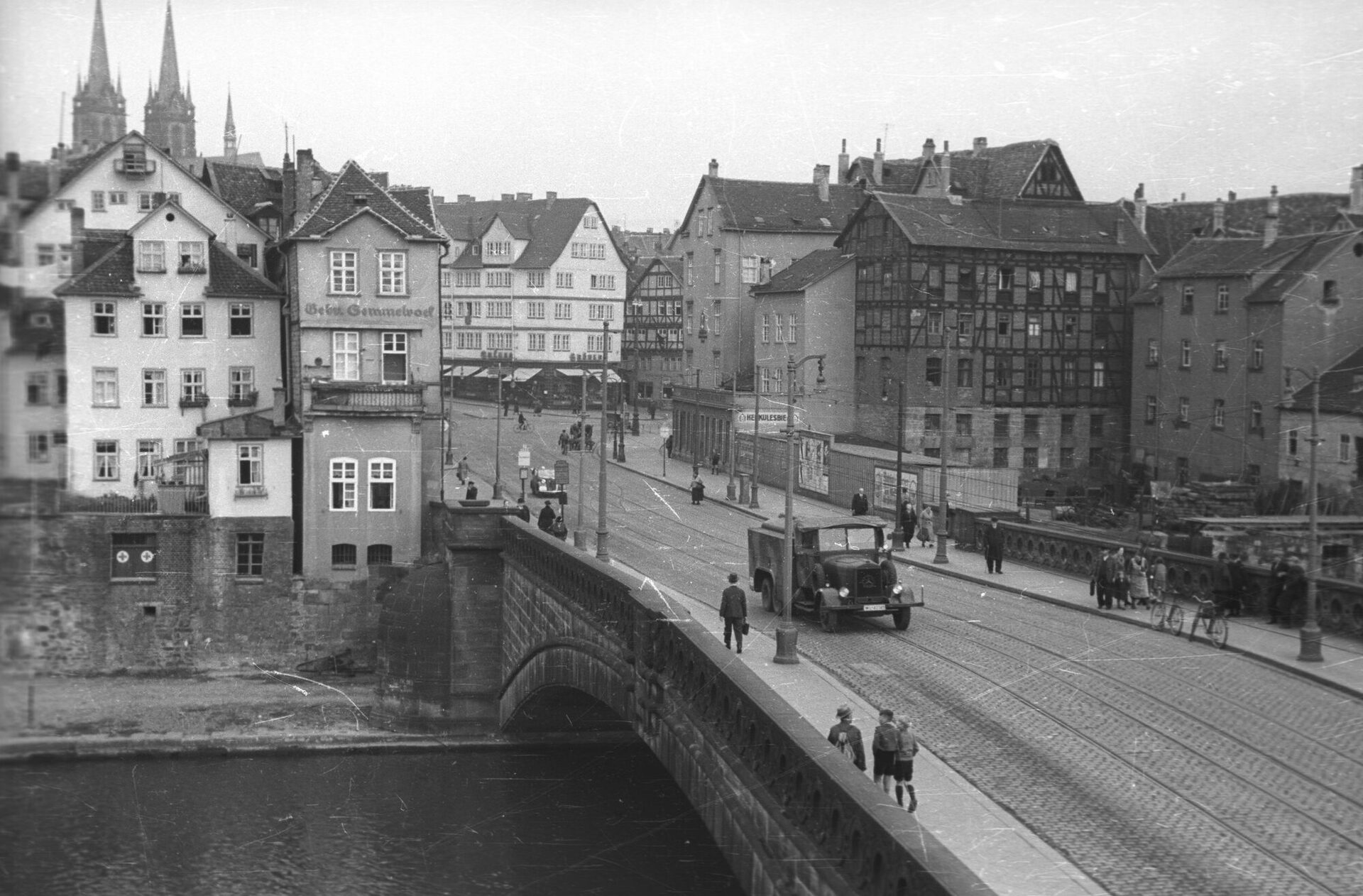 Die stark genutzte Fuldabrücke mit Passanten, einem Lkw und mit auf den Fluss blickenden Menschen mit Blick über Häuser der Altstadt.