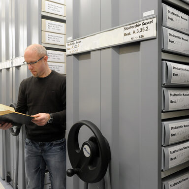 Ein Mann steht zwischen den Archivalien und guckt in ein Buch