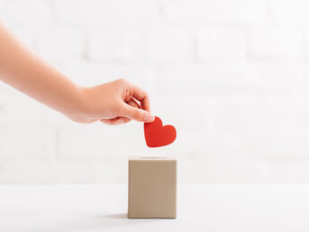 Ausschnitt einer weiblichen Hand, die ein rotes Herz in eine Schachtel wirft, Spendenkonzept