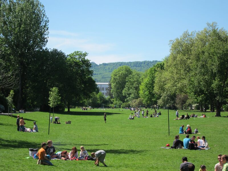 Großer Park mit vielen jungen Menschen, die auf einer großen Wiese sitzen