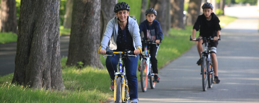Frau im Vordergrund und zwei Jungen im Hintergrund mit Fahrrädern unterwegs