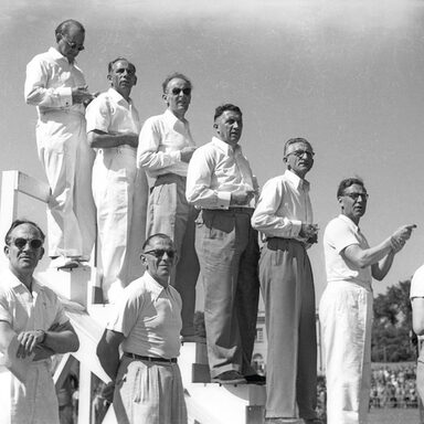 Zu sehen ist das Plakat zur Ausstellung mit einer Schwarzweißfotografie aus den 1950er Jahren, darauf zu sehen ist eine Gruppe von Männern
