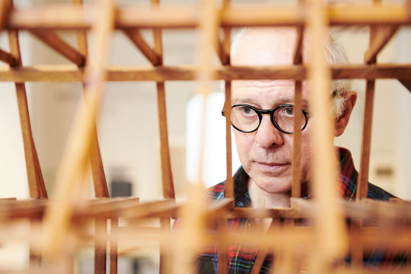 Ein Mensch mit schwarzer Brille schaut durch ein Fachwerkmodell aus Holz