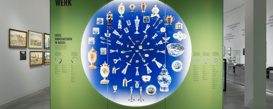 Verschiedene Gegenstände sind in einer großen runden Vitrine auf blauem Hintergrund montiert