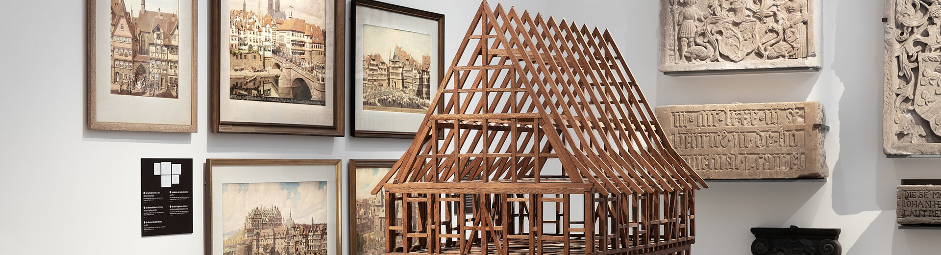 Holzmodell eines Fachwerkhauses, im Hintergrund hängen Bilder in Holzrahmen