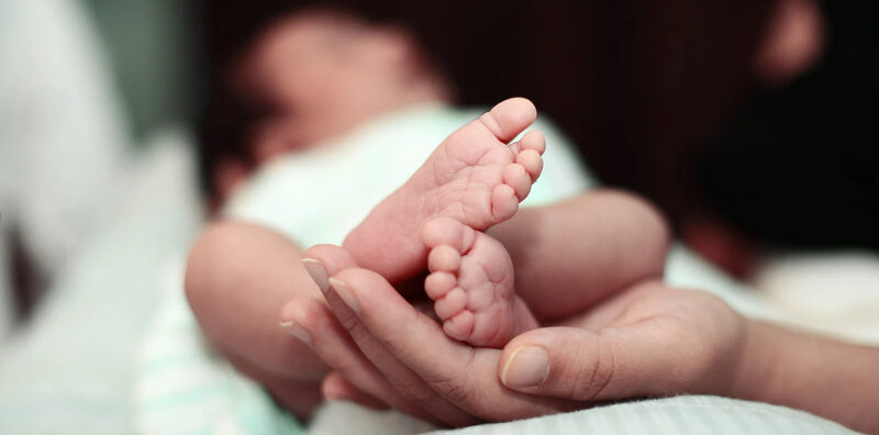 Füße eines Neugeborenen in der Hand eines Erwachsenen.