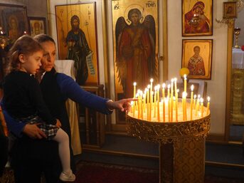Frau mit einem Kind auf dem Arm vor einer Schale mit Kerzen