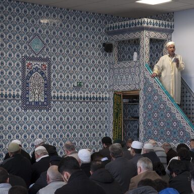 Iman der sunnitischen Moscheegemeinde mit knienden Männern im Vordergrund
