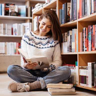 Frau sitzt vor einem Bücherregal auf dem Boden und liest ein Buch