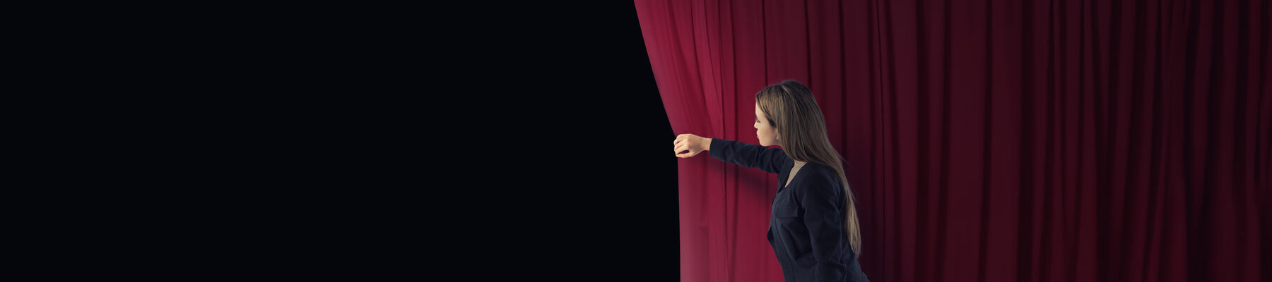Frau, die einen roten Vorhang auf einer Theaterbühne zur Seite zieht.