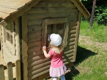 Ein kleines Mädchen steht vor einer Holzhütte