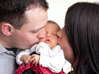 Ein neugeborenes Baby wird von ihrem Vater und Mutter auf die Wange geküsst